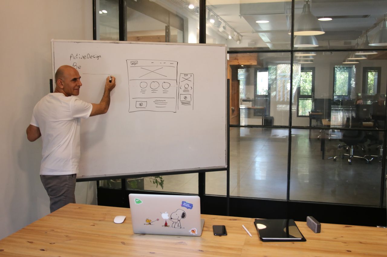 The Art of Drawing Readers In: Your attractive post title goes here Side view of middle aged male leader in white t shirt writing on whiteboard during presentation in modern office space with glass walls